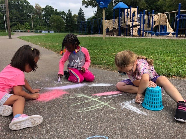 Three children drawing with chalk on pavement