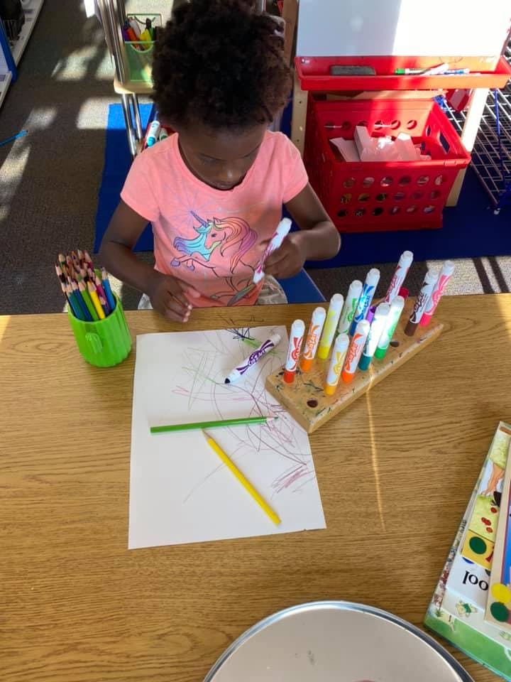 Child drawing on paper with markers at a table