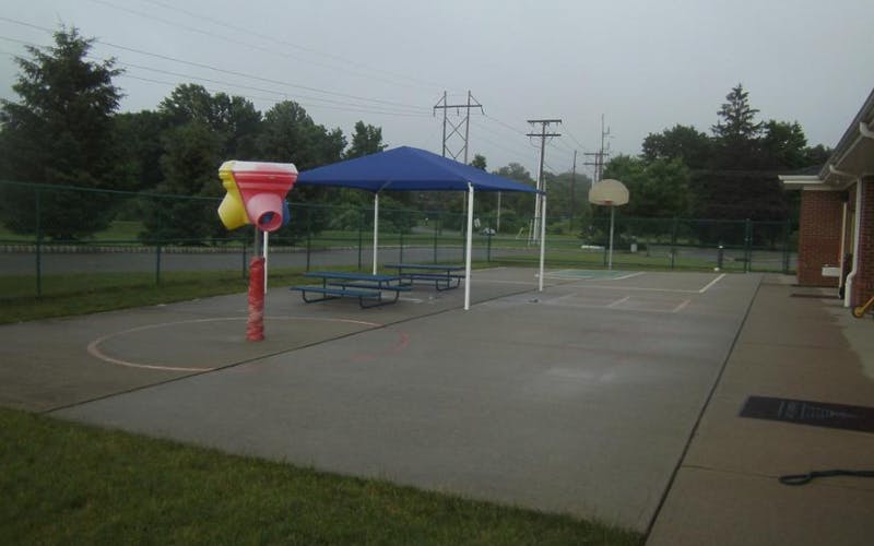Outdoor play area with a colorful water feature, picnic tables under a canopy, and a basketball hoop