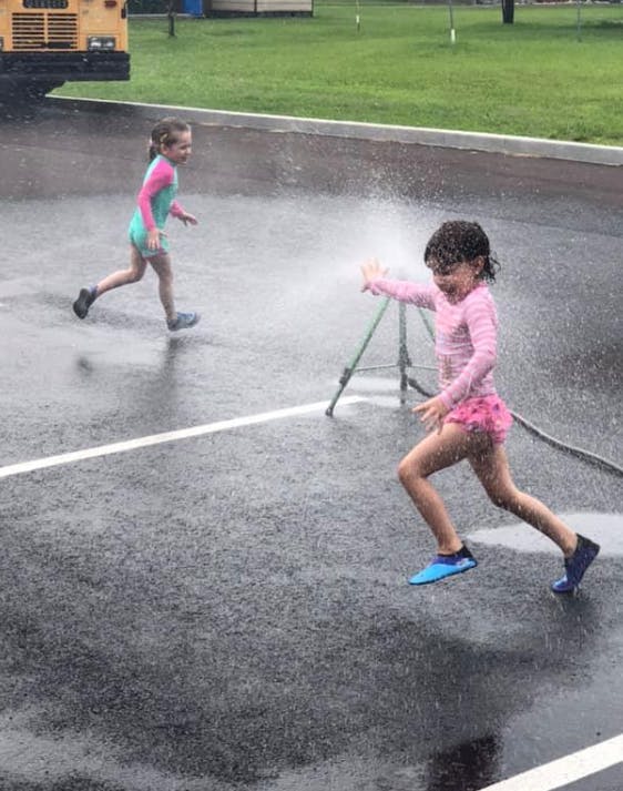 Two children running through sprinkler water on pavement