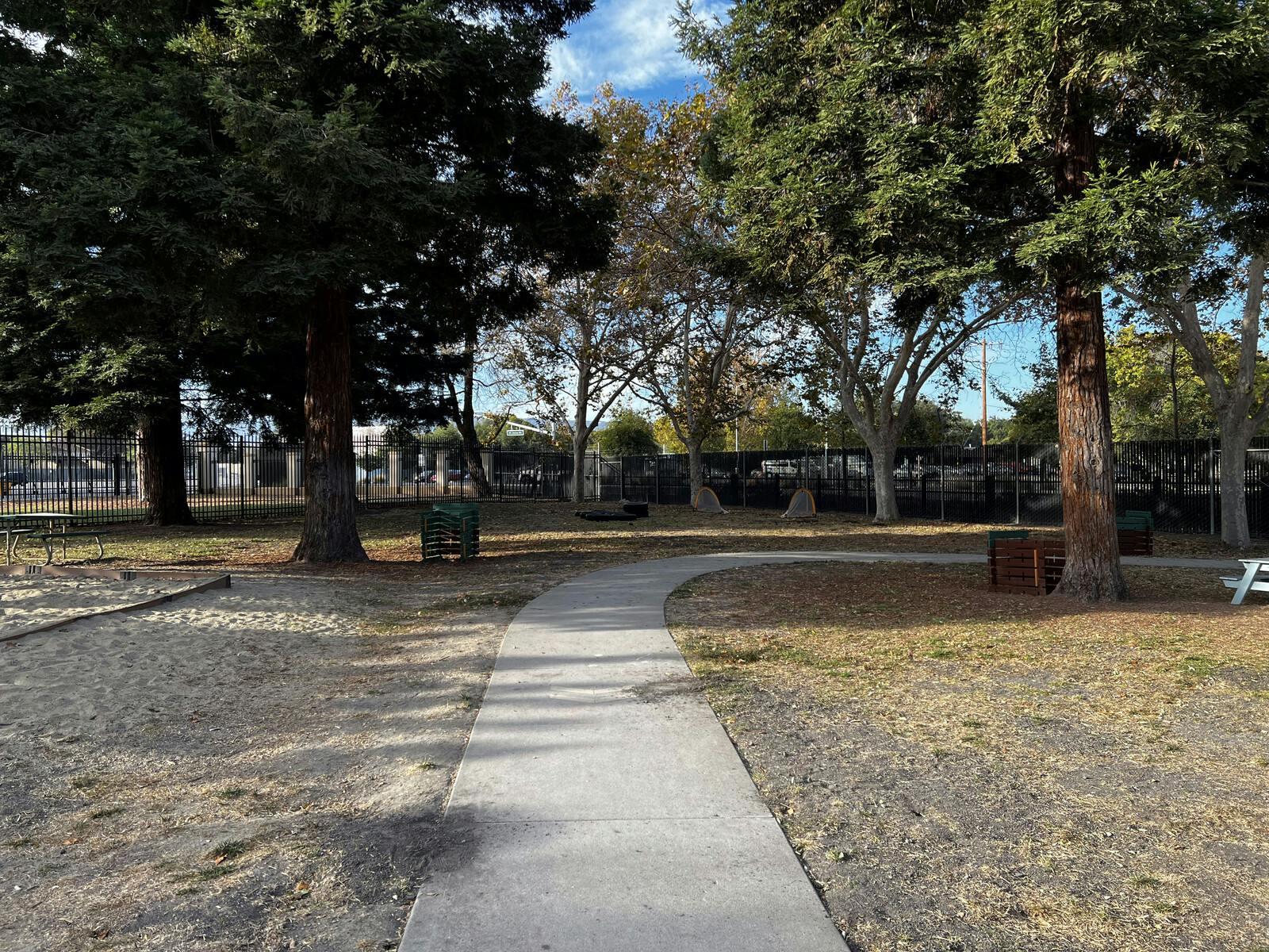 Curved concrete path through a park with trees and dry grass