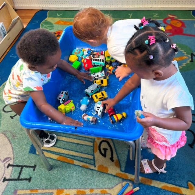Three children playing with toy vehicles in a blue water table