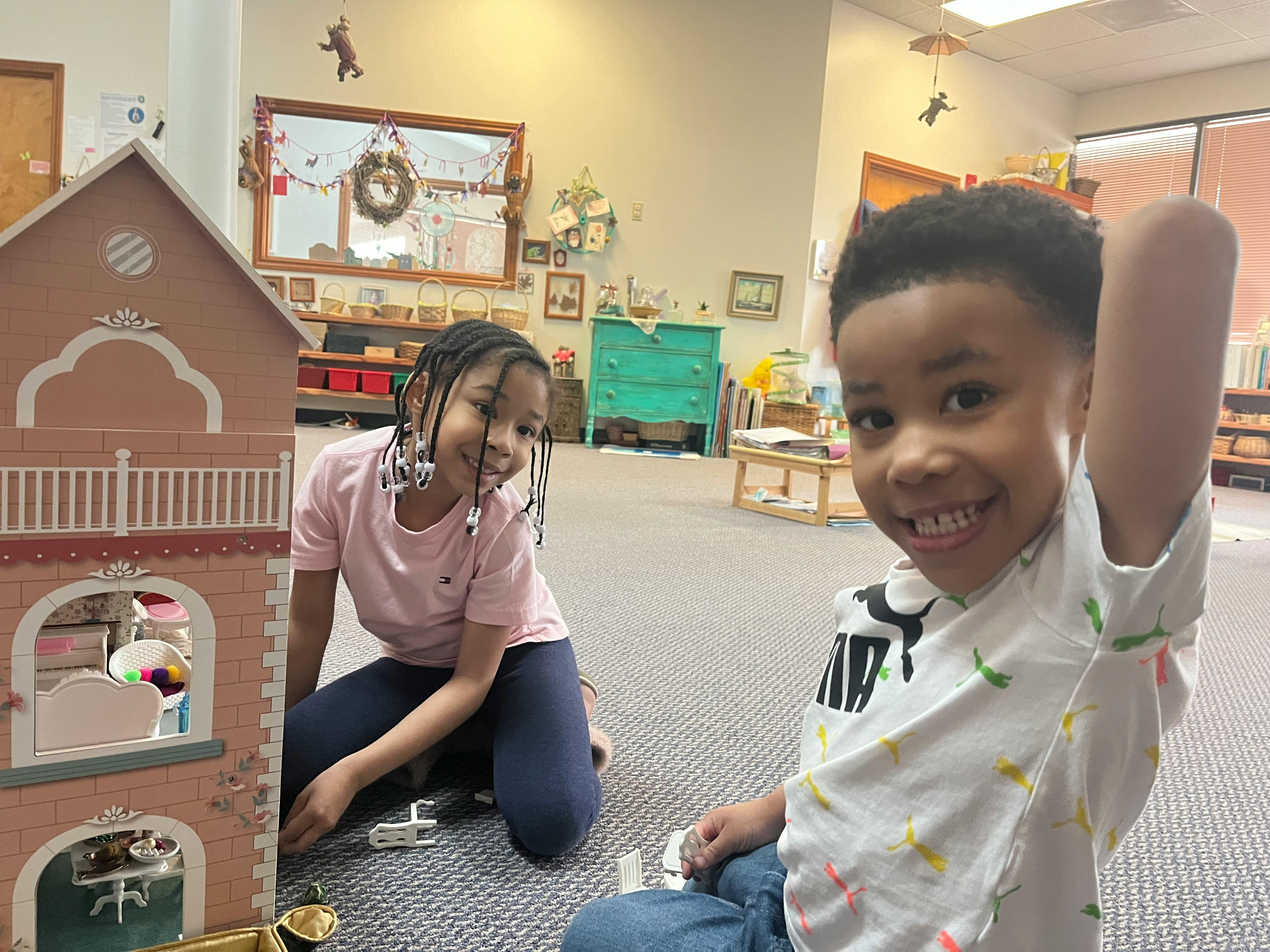 Two children playing with a dollhouse on the floor