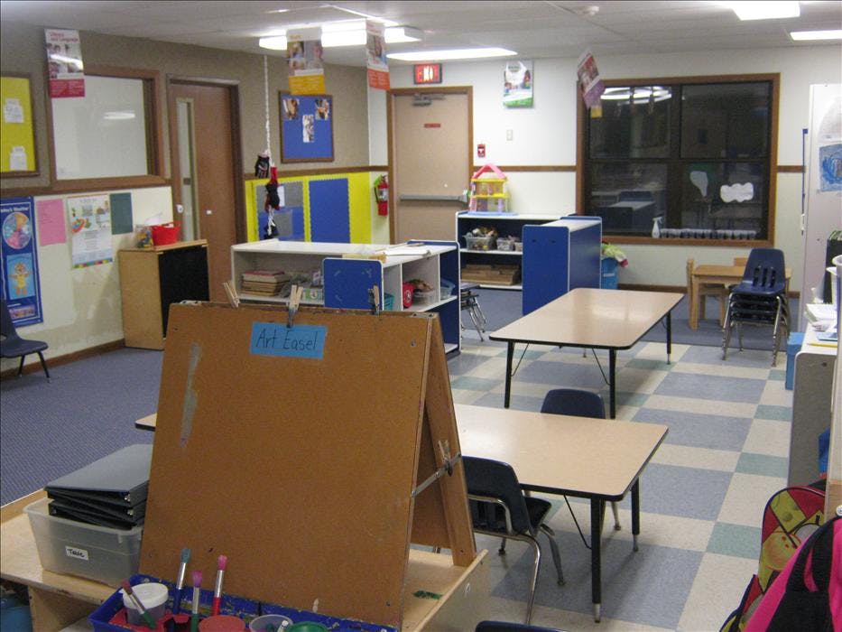 Classroom with child-sized tables and chairs, shelves, and an art easel