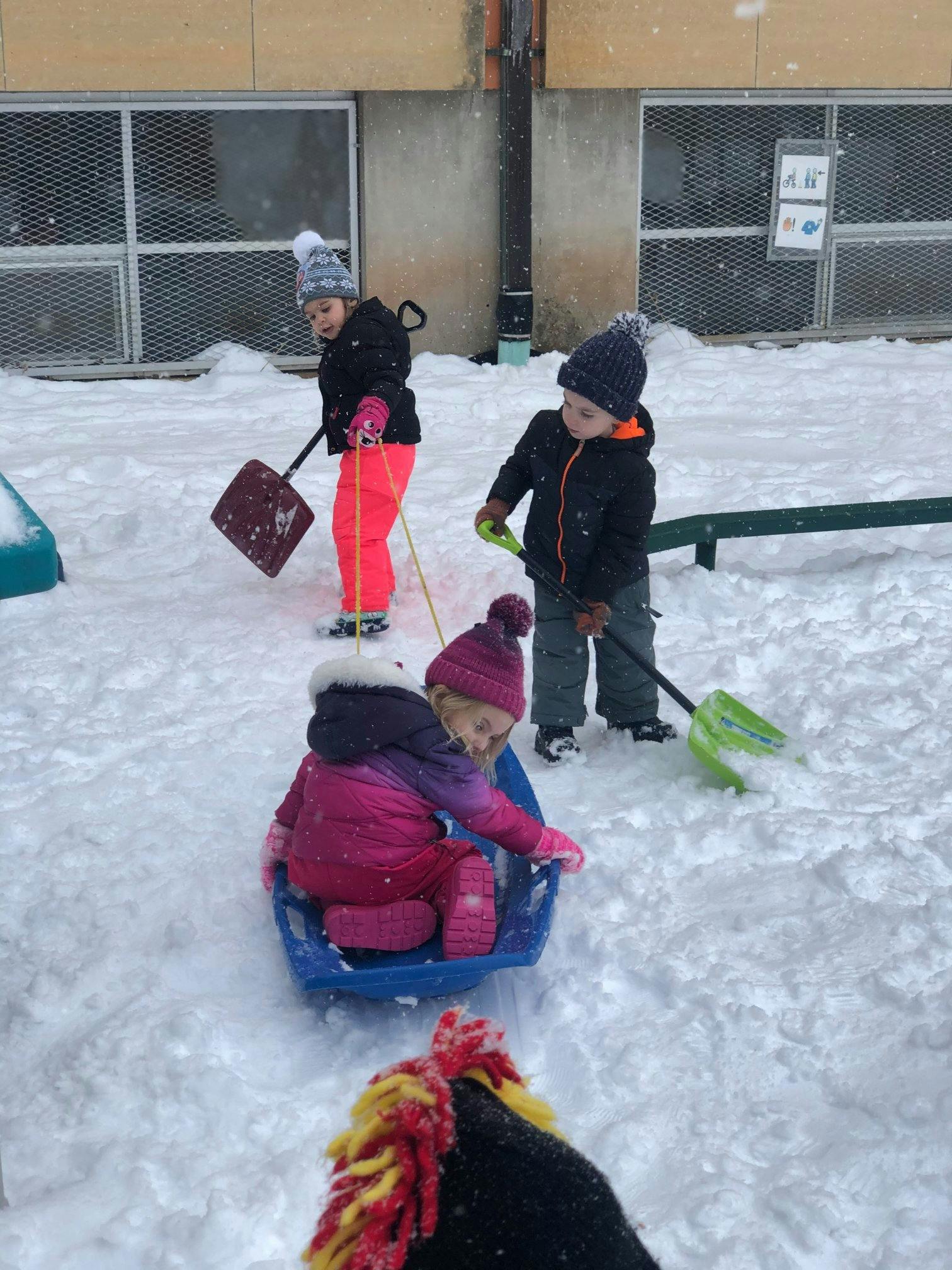 Children playing in snow with shovels and a sled