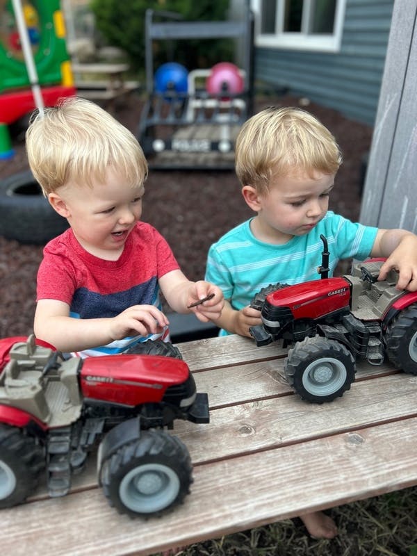Two children playing with toy tractors on a wooden surface