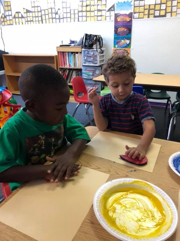 Two children doing an art activity at a table in a classroom