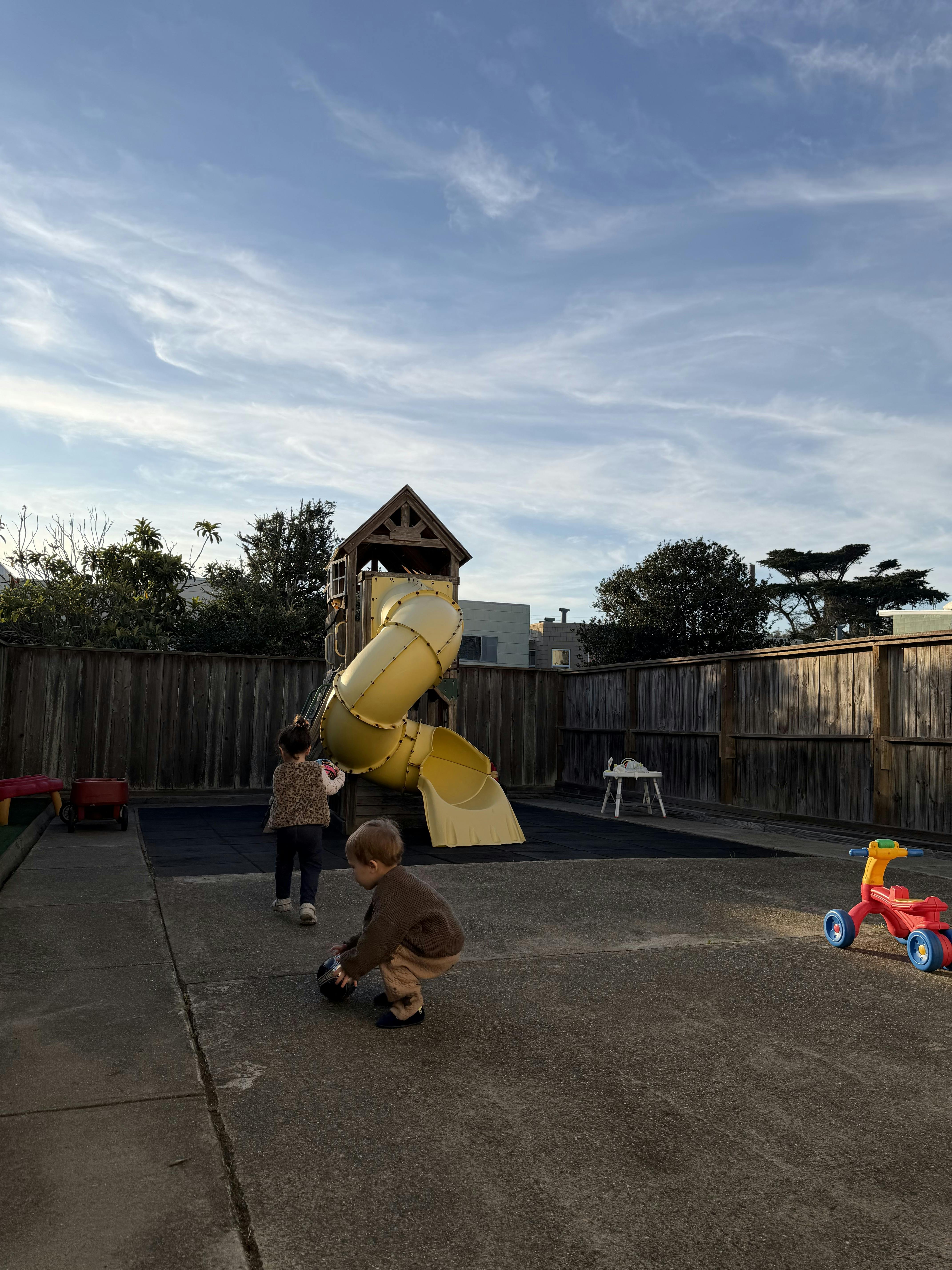 Two children playing on a playground next to a yellow slide structure