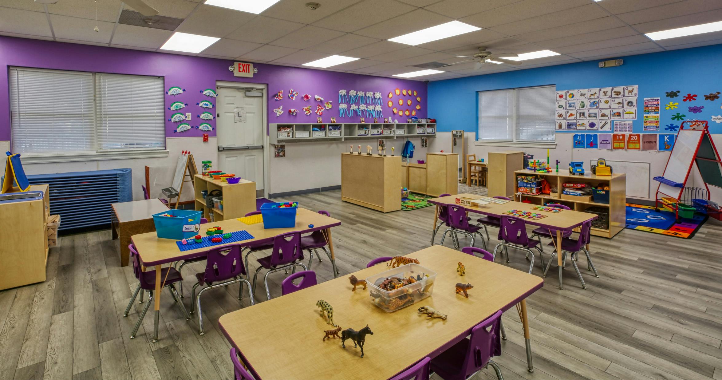 A colorful empty classroom with tables, chairs, and learning materials