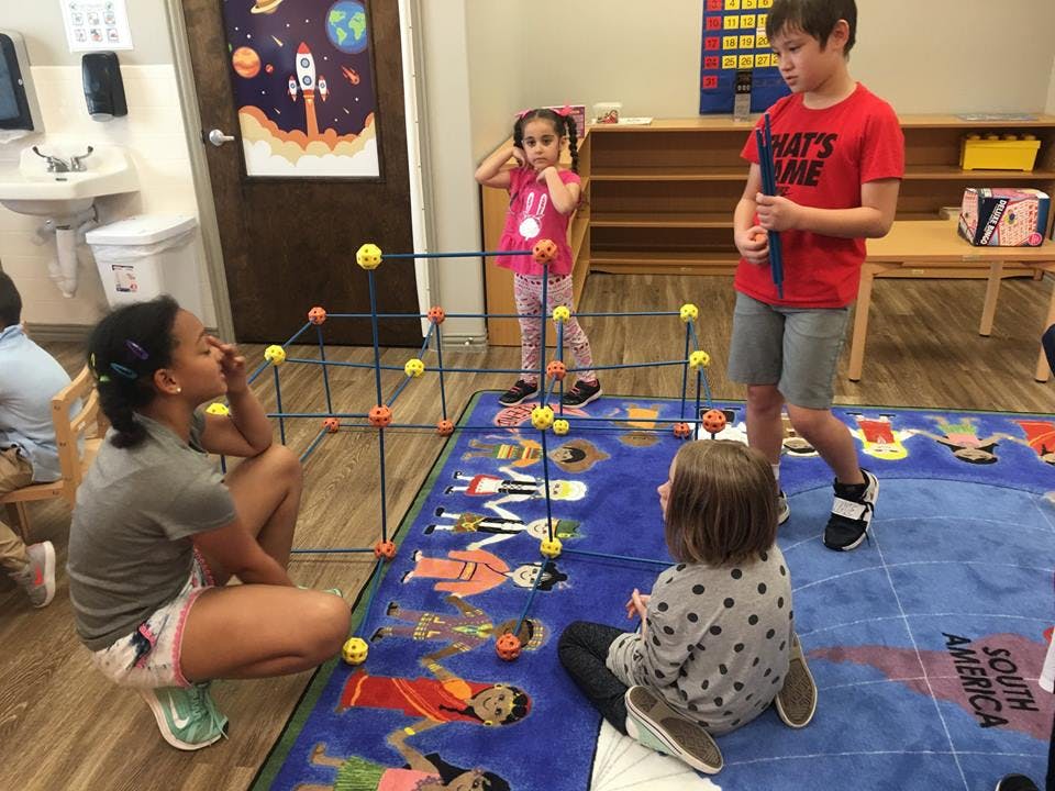 Children playing with a building toy on a rug in a classroom