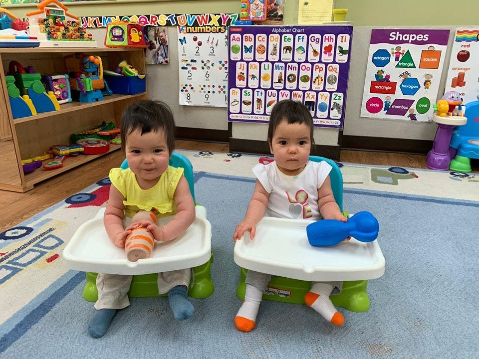 Two children sitting in high chairs in a classroom