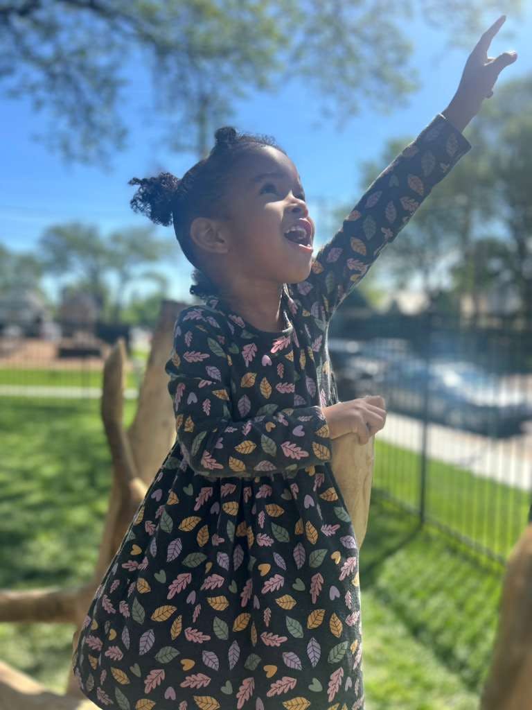 Child in a leaf-patterned dress pointing toward the sky outdoors