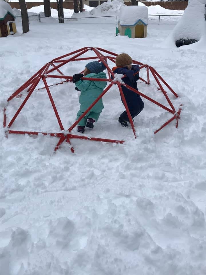 Two children climbing on a red geodesic dome in the snow