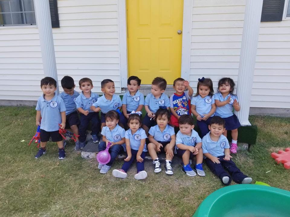 Group of children sitting and standing in front of a building with a yellow door
