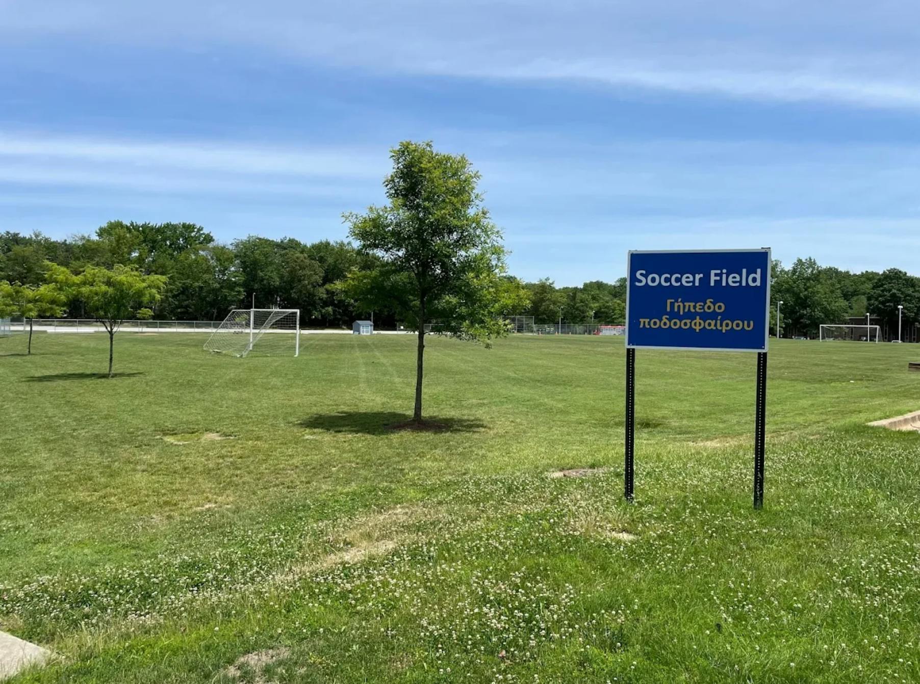 Soccer field sign with trees and goalposts in the background