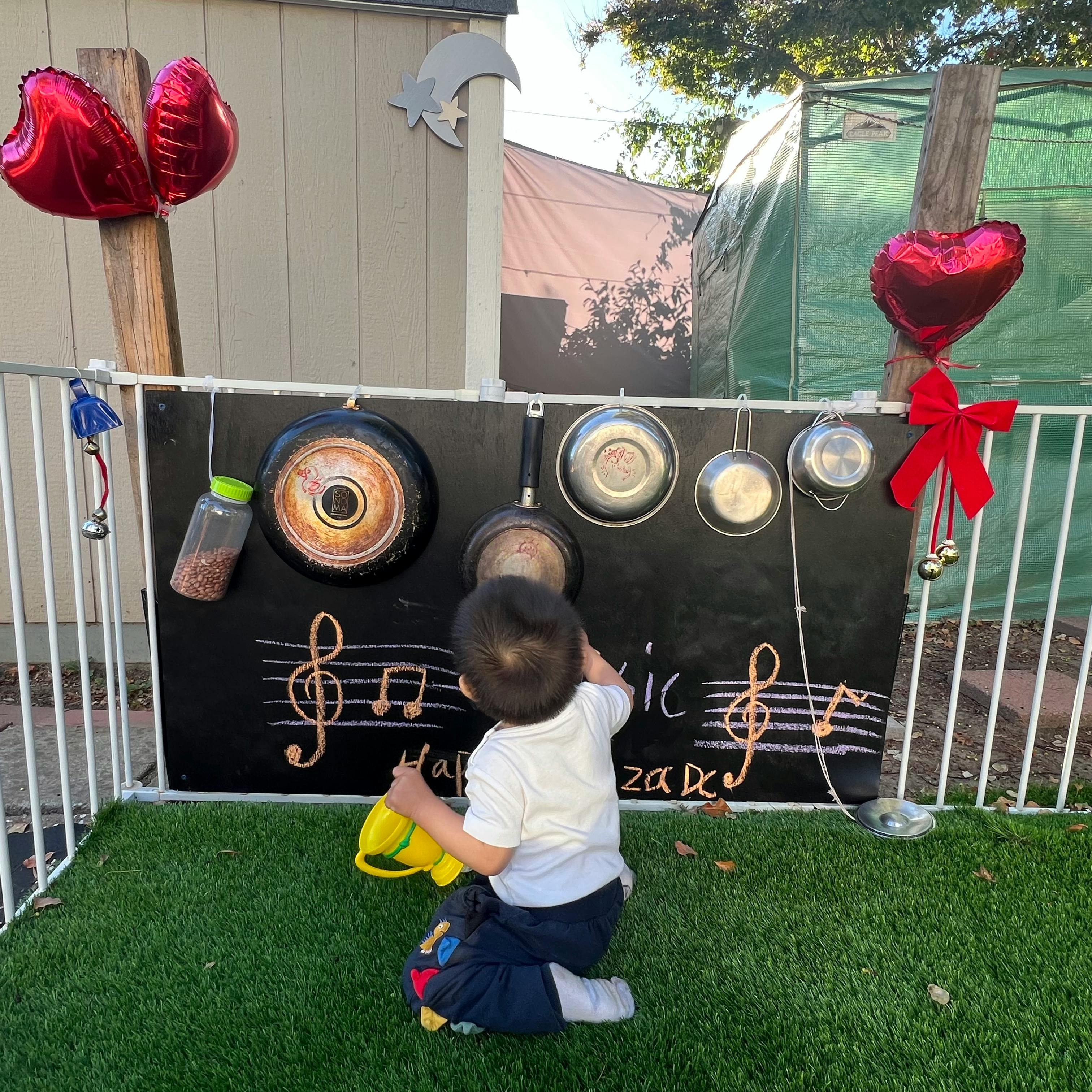 Child playing with kitchen utensils hanging on a chalkboard music wall