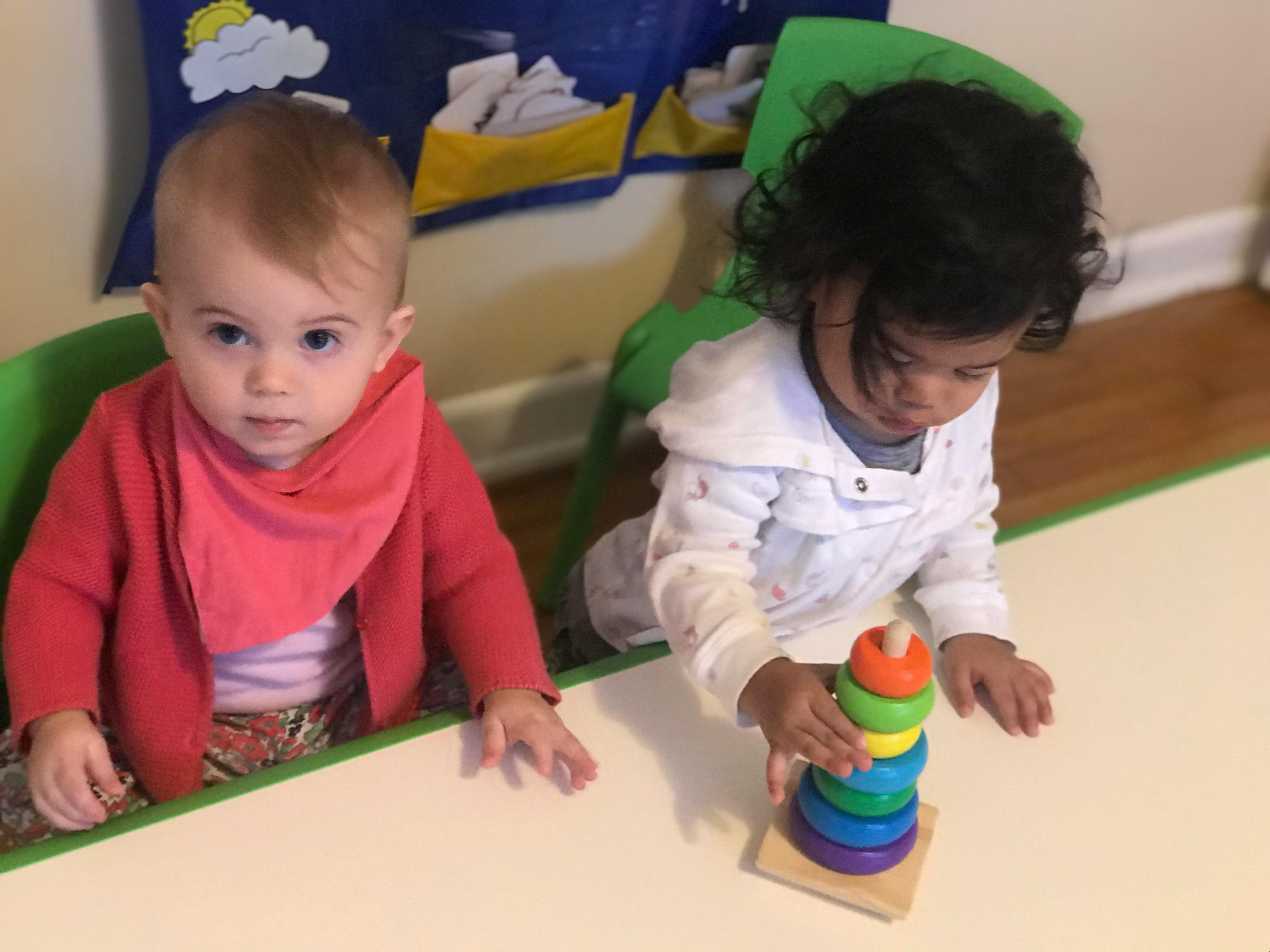 Two children at a table, one looking forward, one playing with a stacking toy