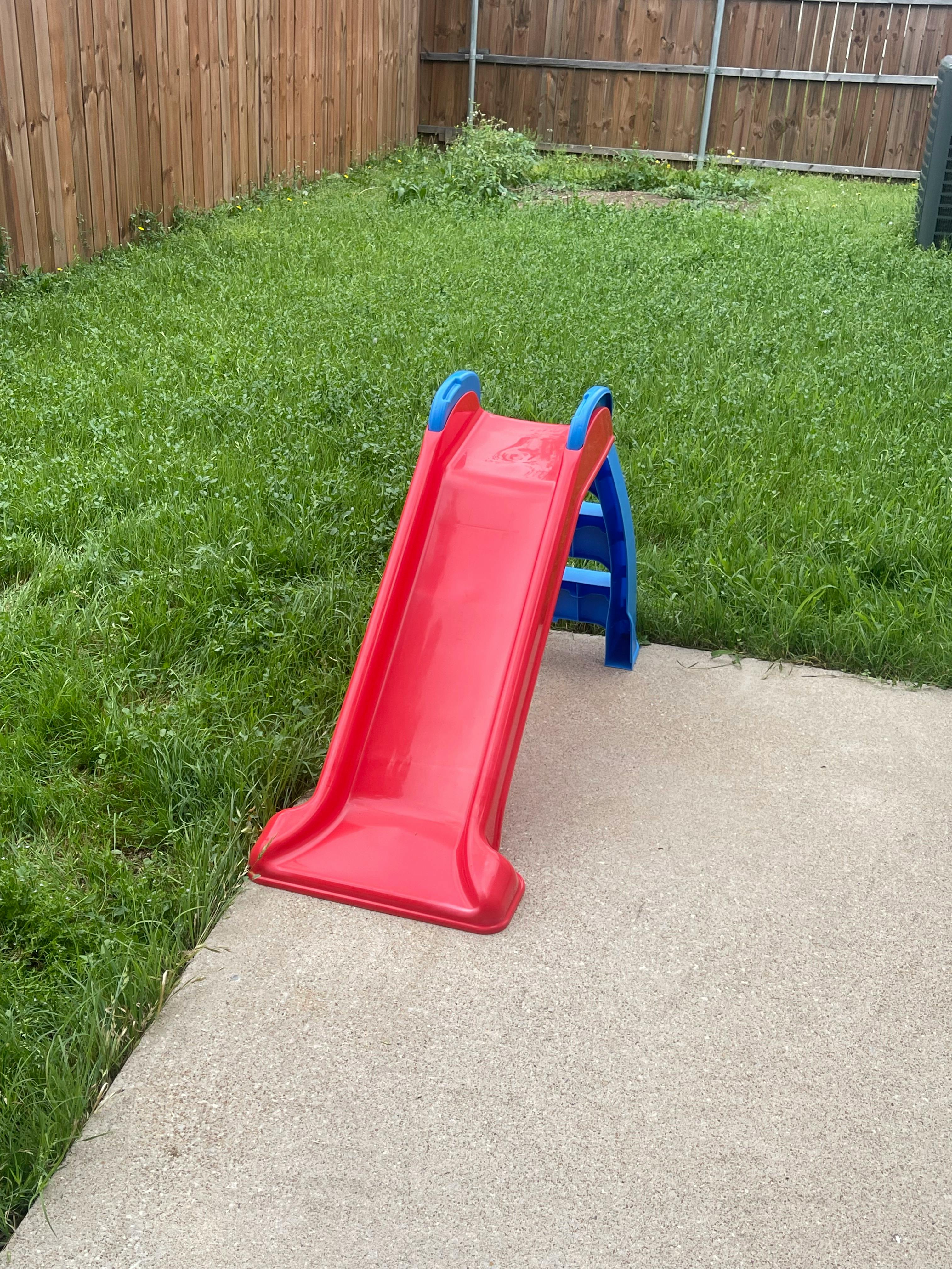 Red and blue child's slide on concrete next to grass