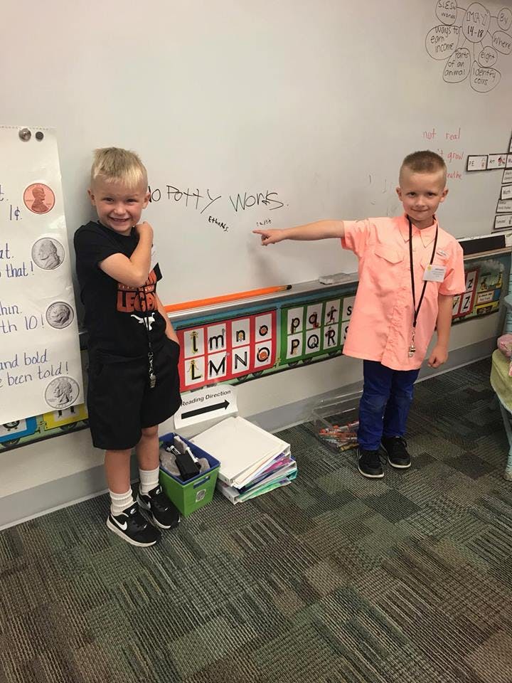 Two children standing in front of a whiteboard, one pointing at text