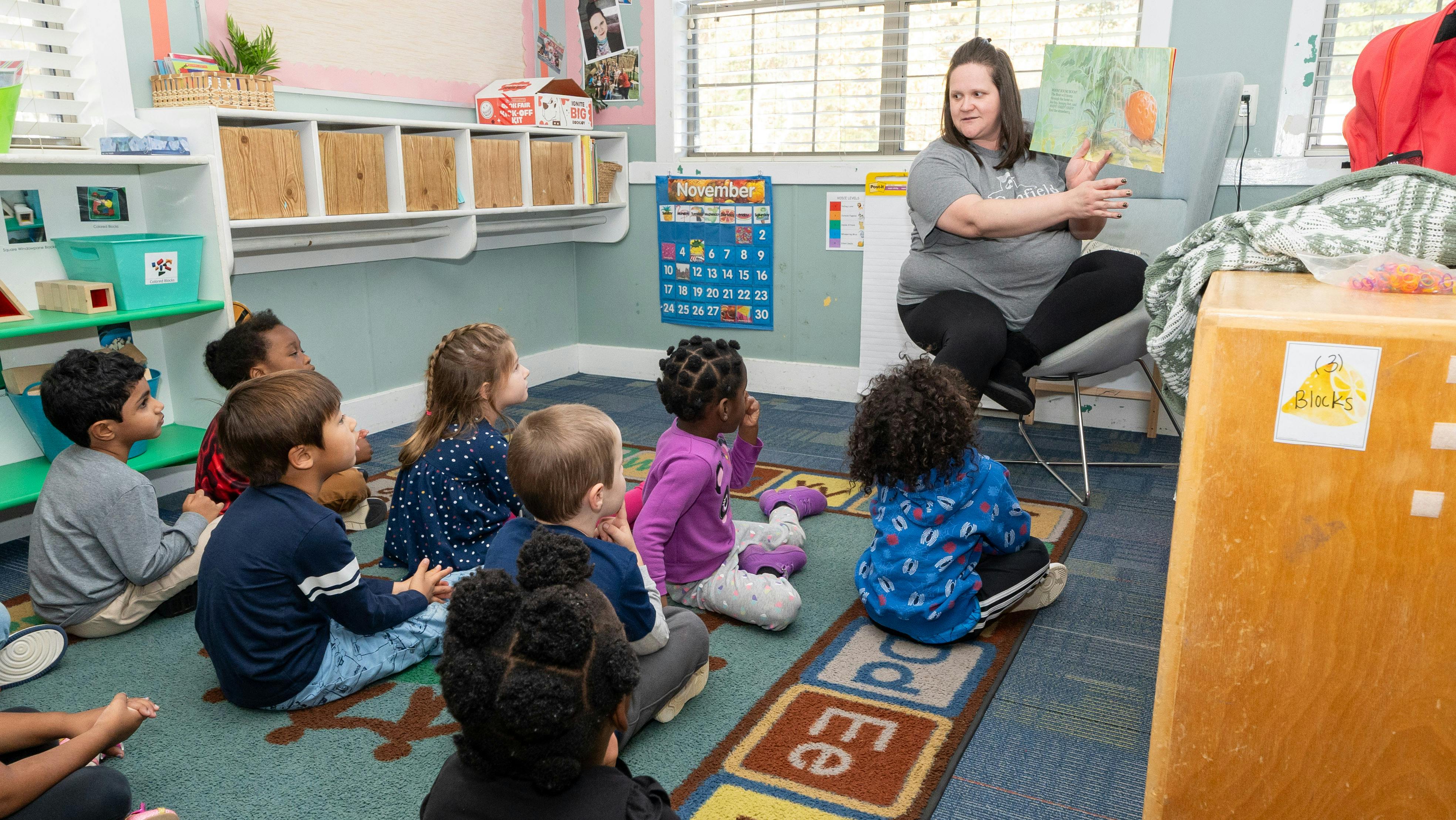 Adult reading a book to a group of children sitting on the floor