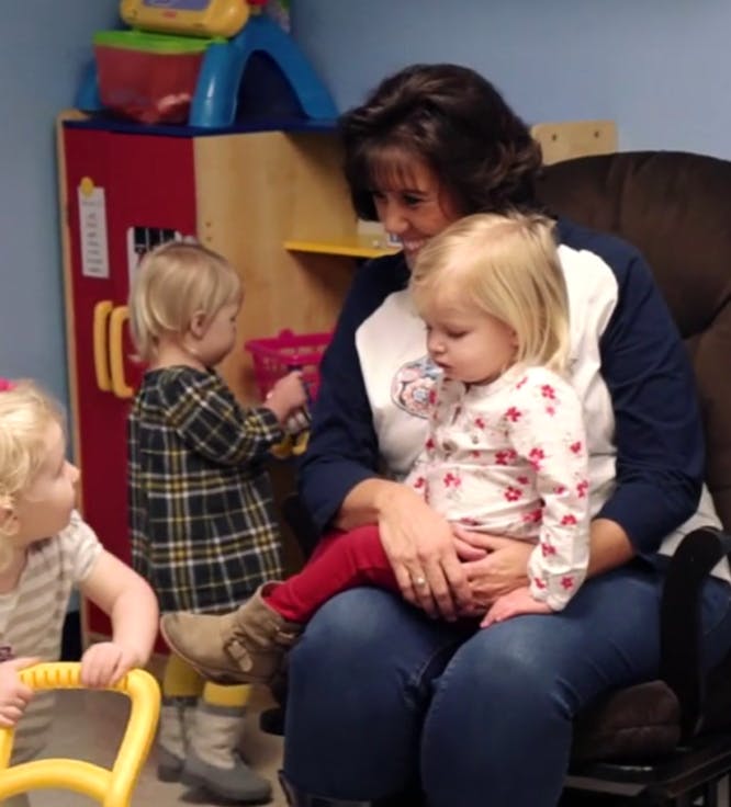 Person sitting with a child on lap, another child standing nearby