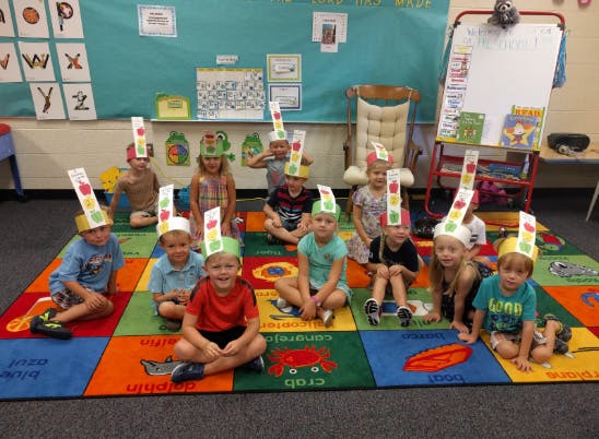 Group of children wearing paper hats sitting on a colorful rug