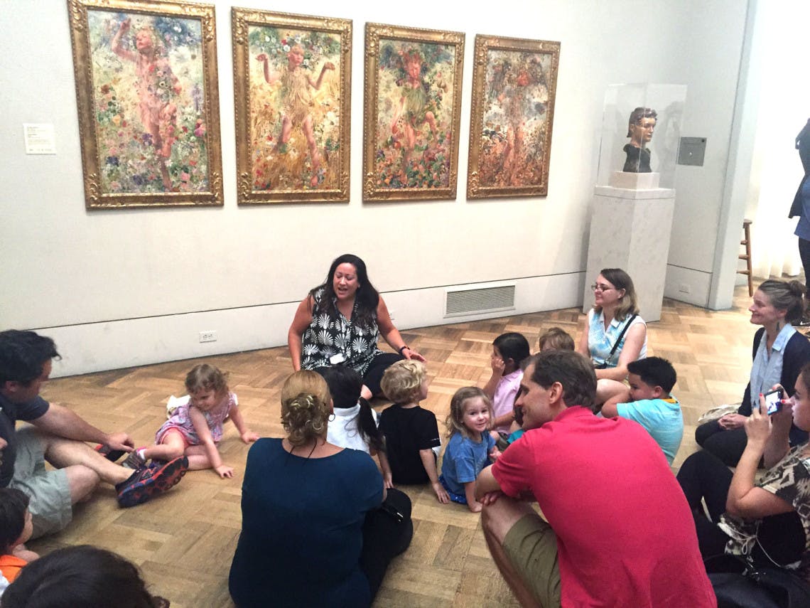 Adults and children sitting on the floor in a museum looking at paintings