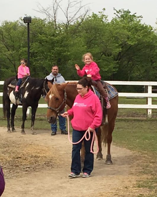 Person leading a horse with a child riding, another child on a horse in background