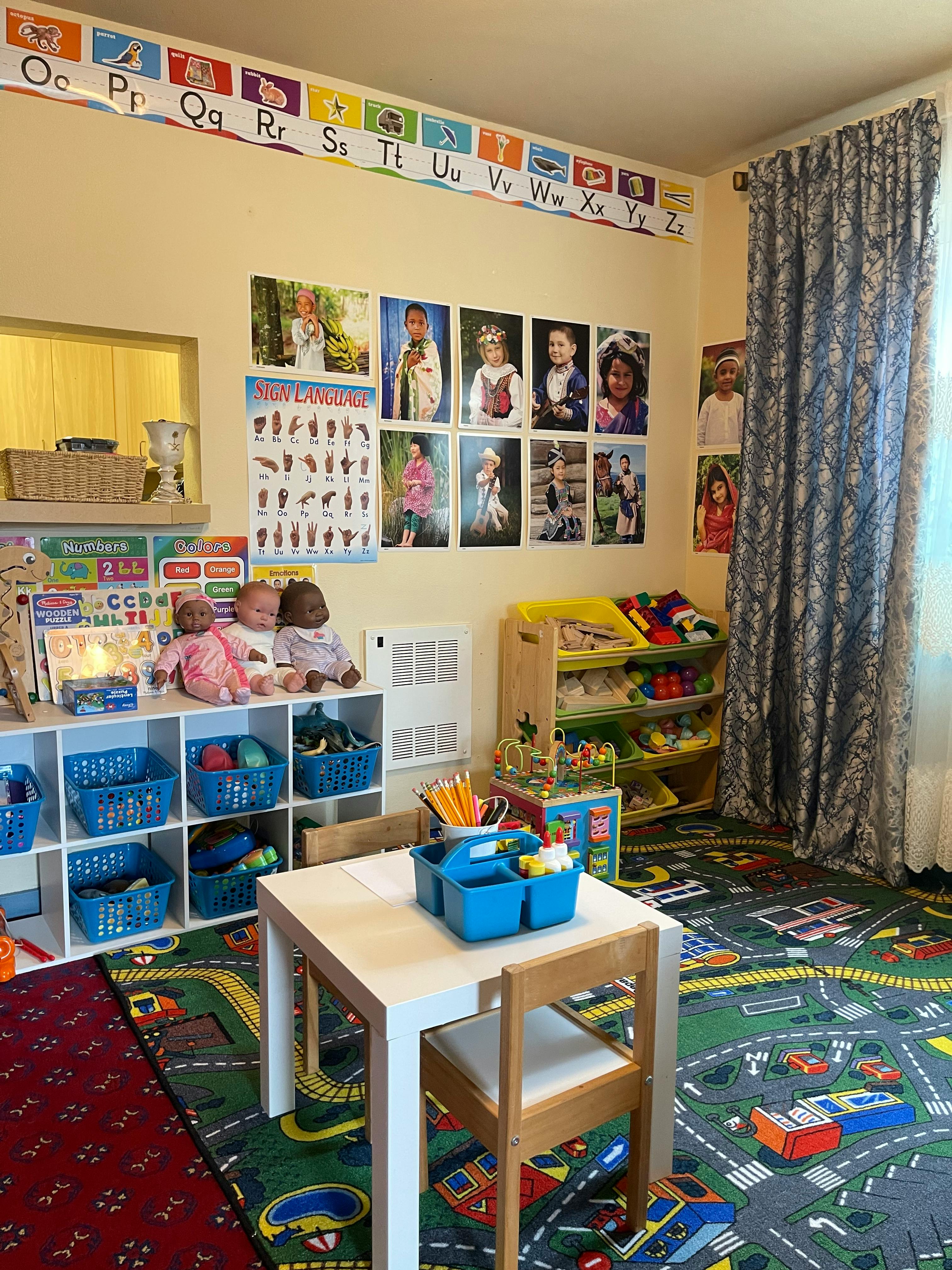 Classroom with alphabet border, photos on wall, shelves with baskets, and small table with chair