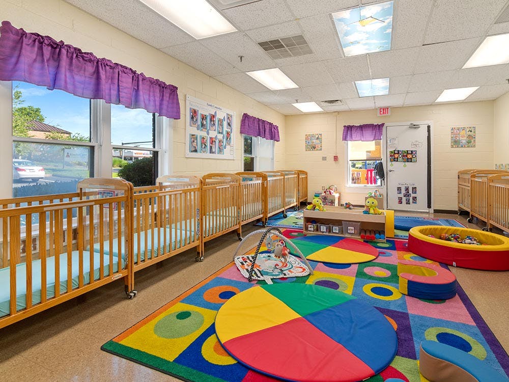 Cribs and play area with colorful rug in a daycare room