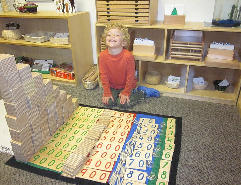 Child kneeling next to a math learning mat with number blocks