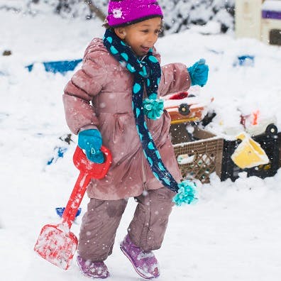 Child in winter clothes holding a red shovel in the snow