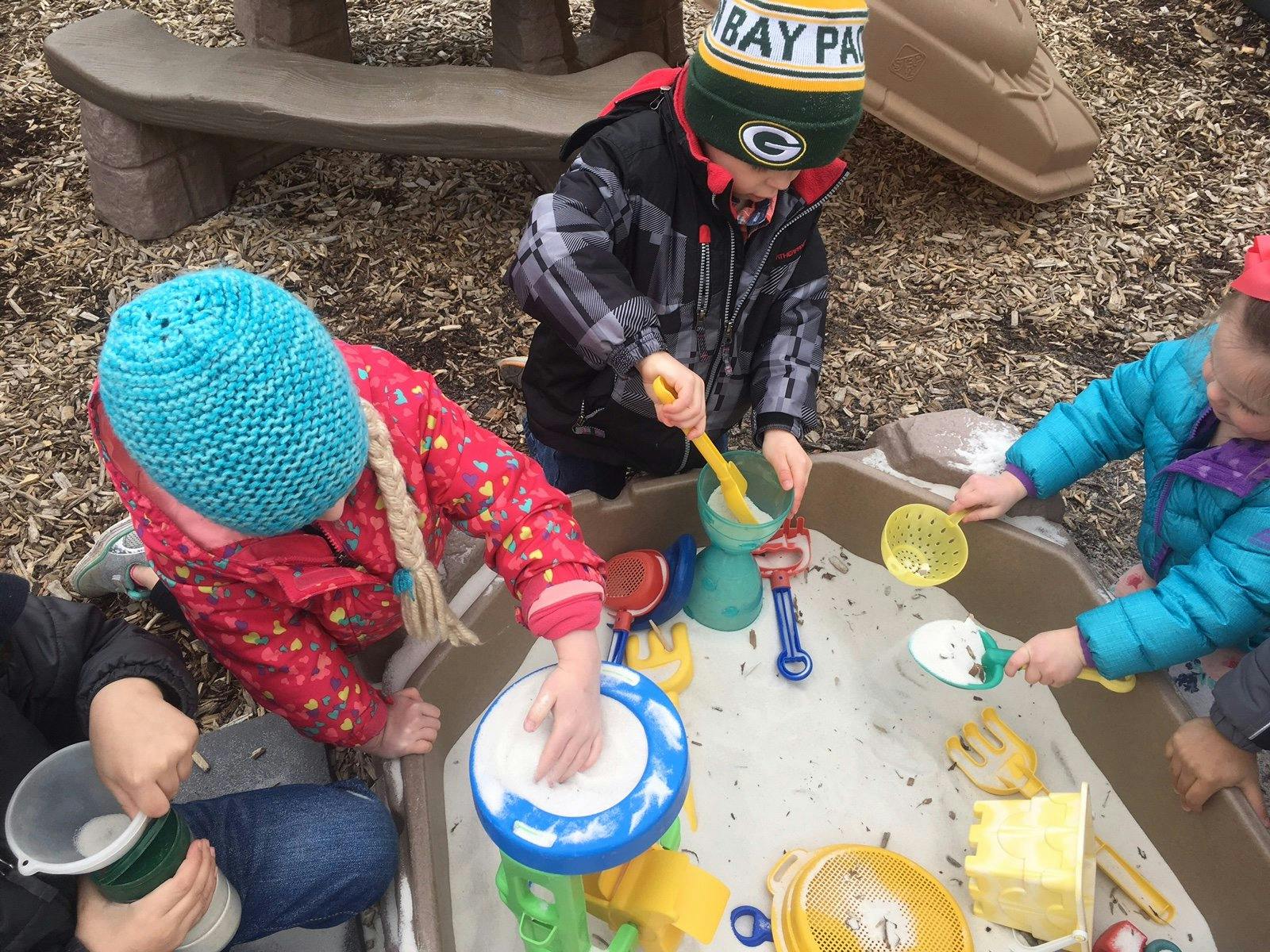 Three children playing with sand and toys in a sand table