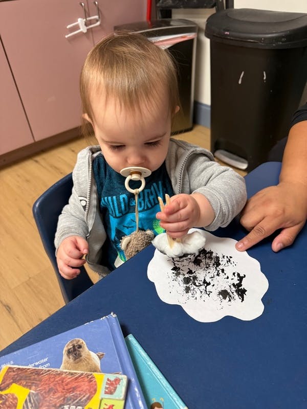 Child using a clothespin and cotton ball to paint on a paper cloud