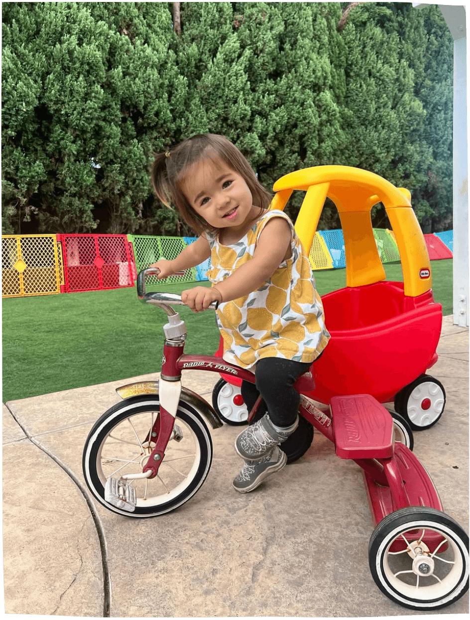 Child on a tricycle with a red wagon attached