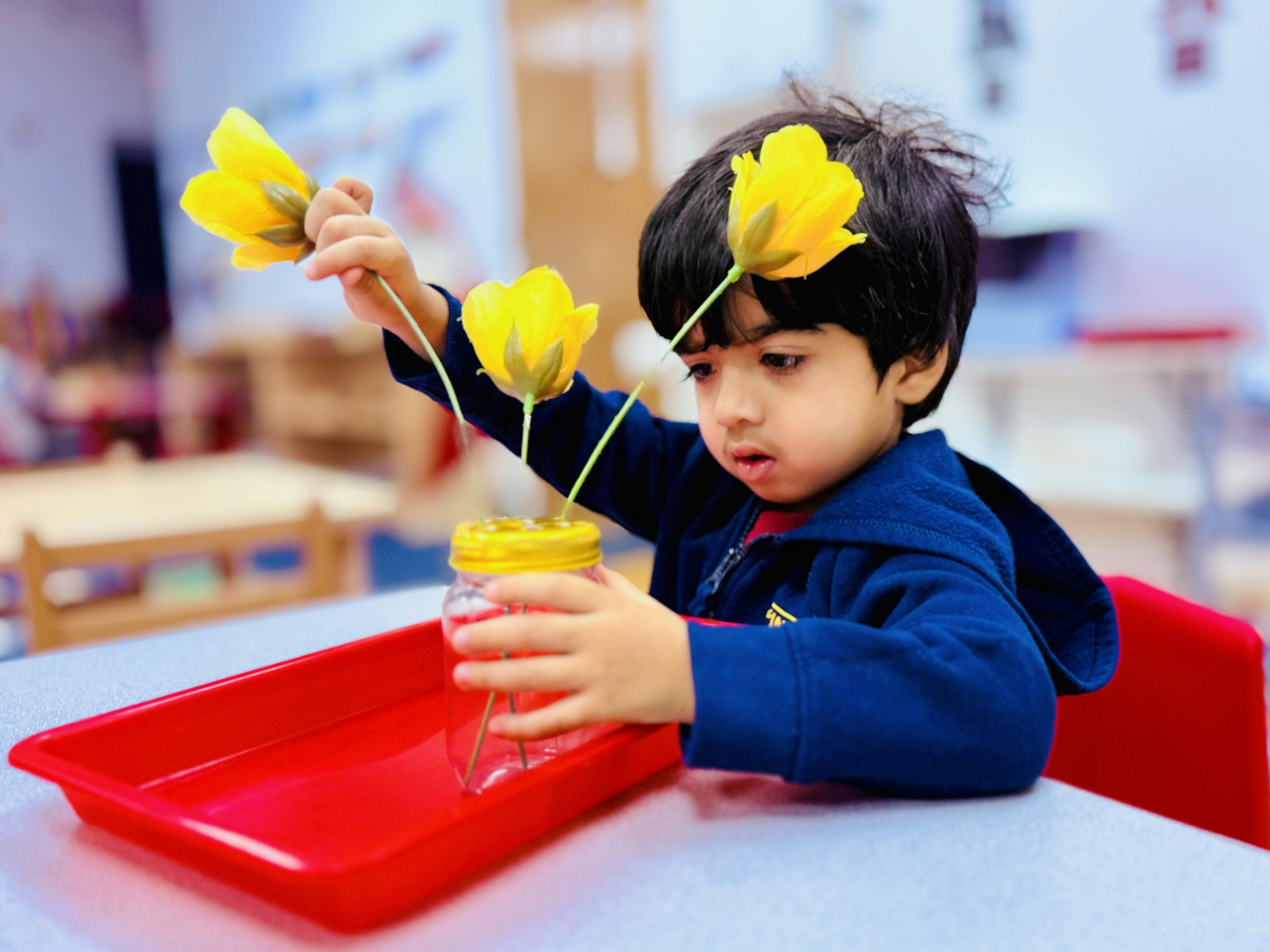 Child placing yellow flowers into a jar on a red tray