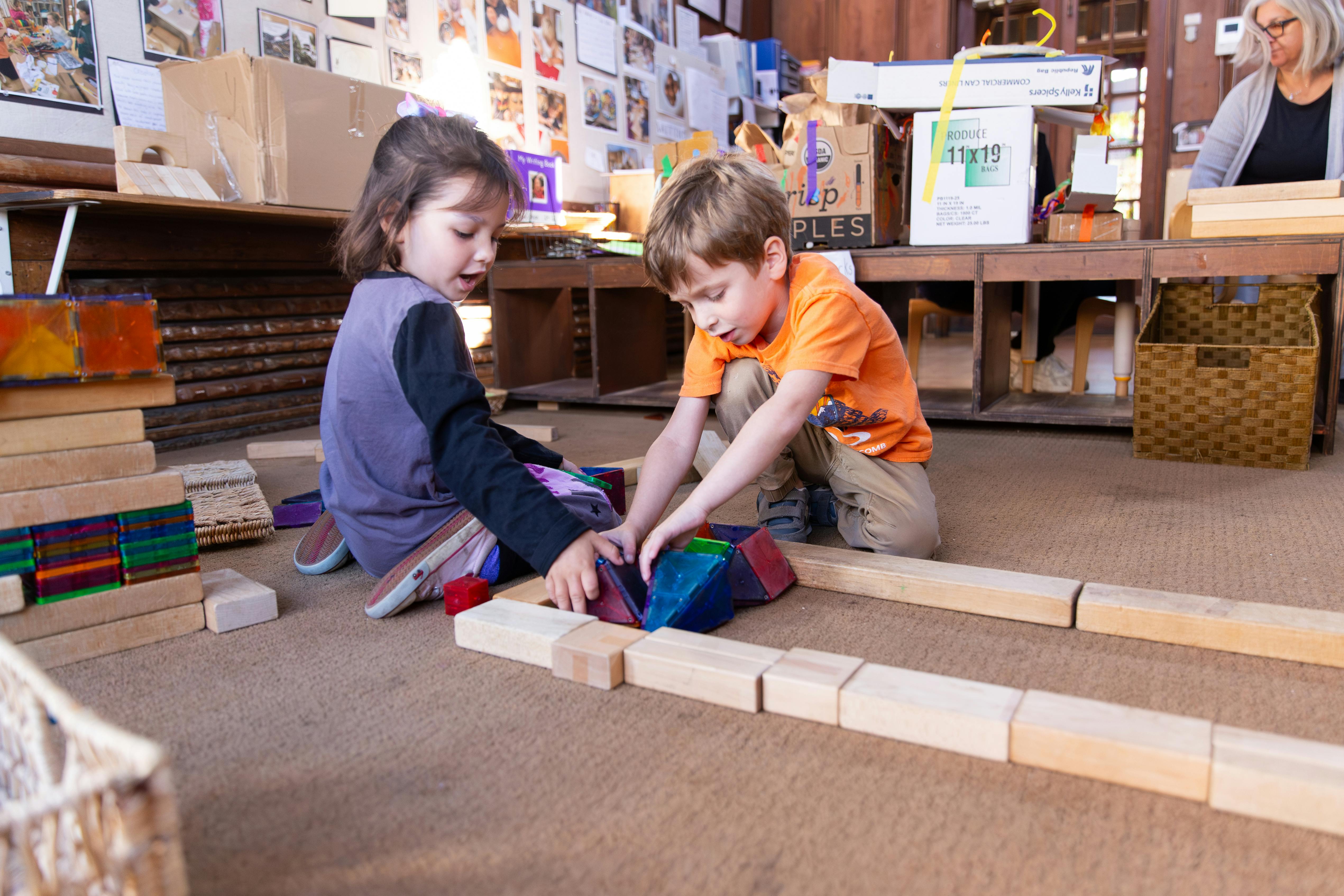 Two children building with magnetic and wooden blocks on a classroom floor