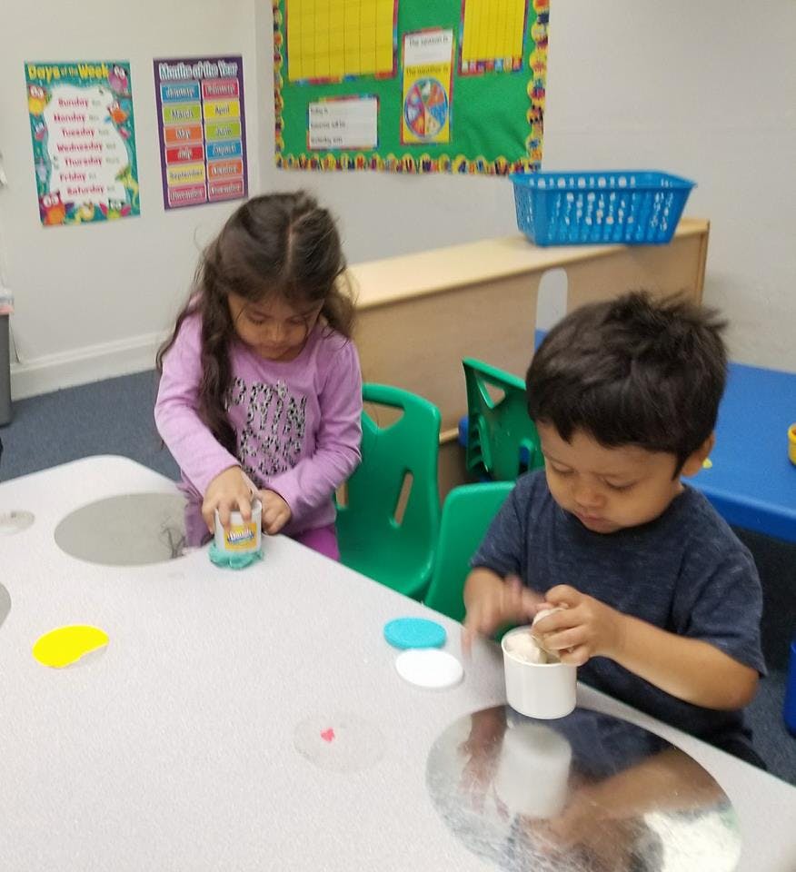 Two children playing with objects at a table in a classroom