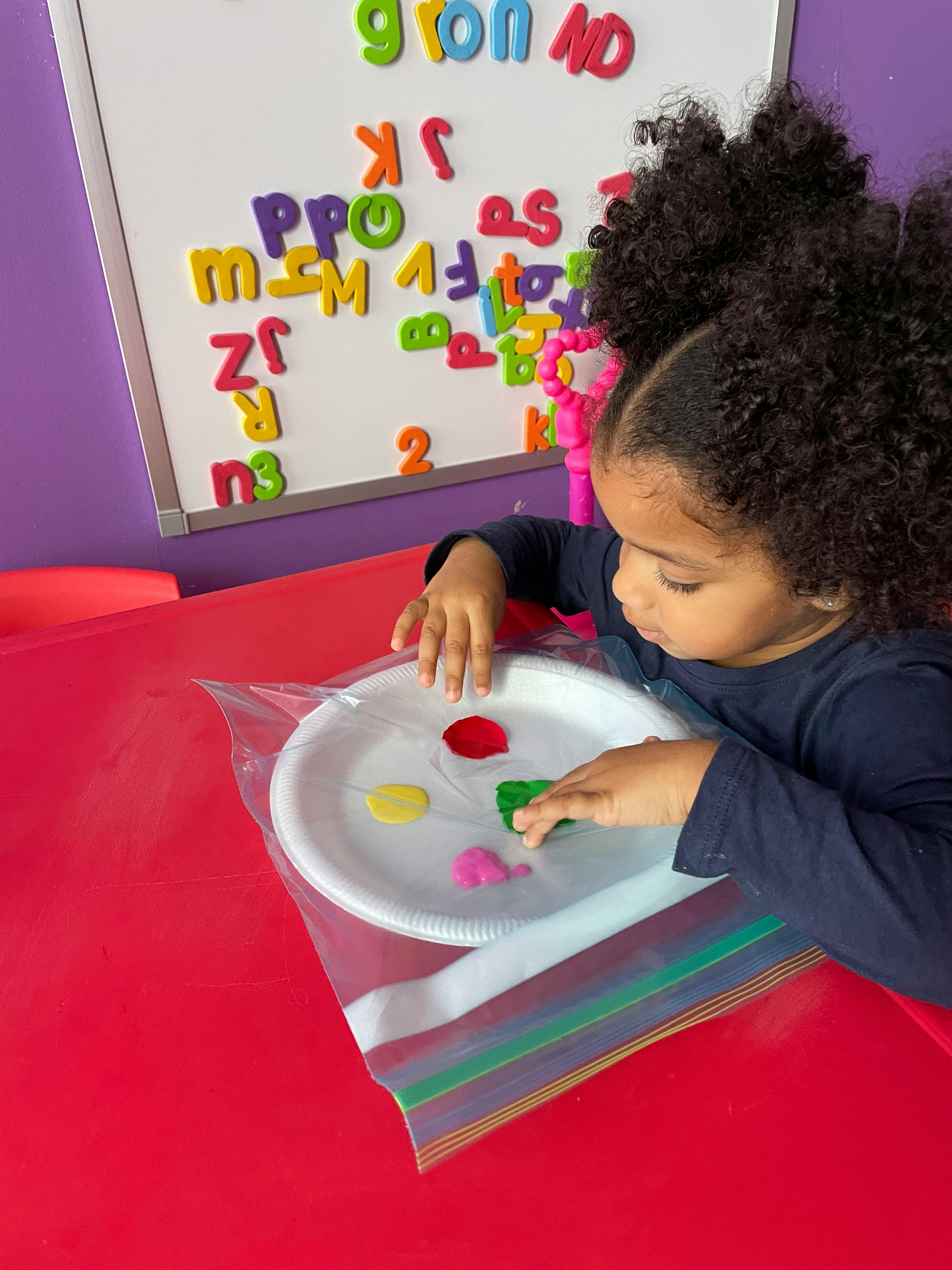 Child playing with paint on a paper plate inside a plastic bag