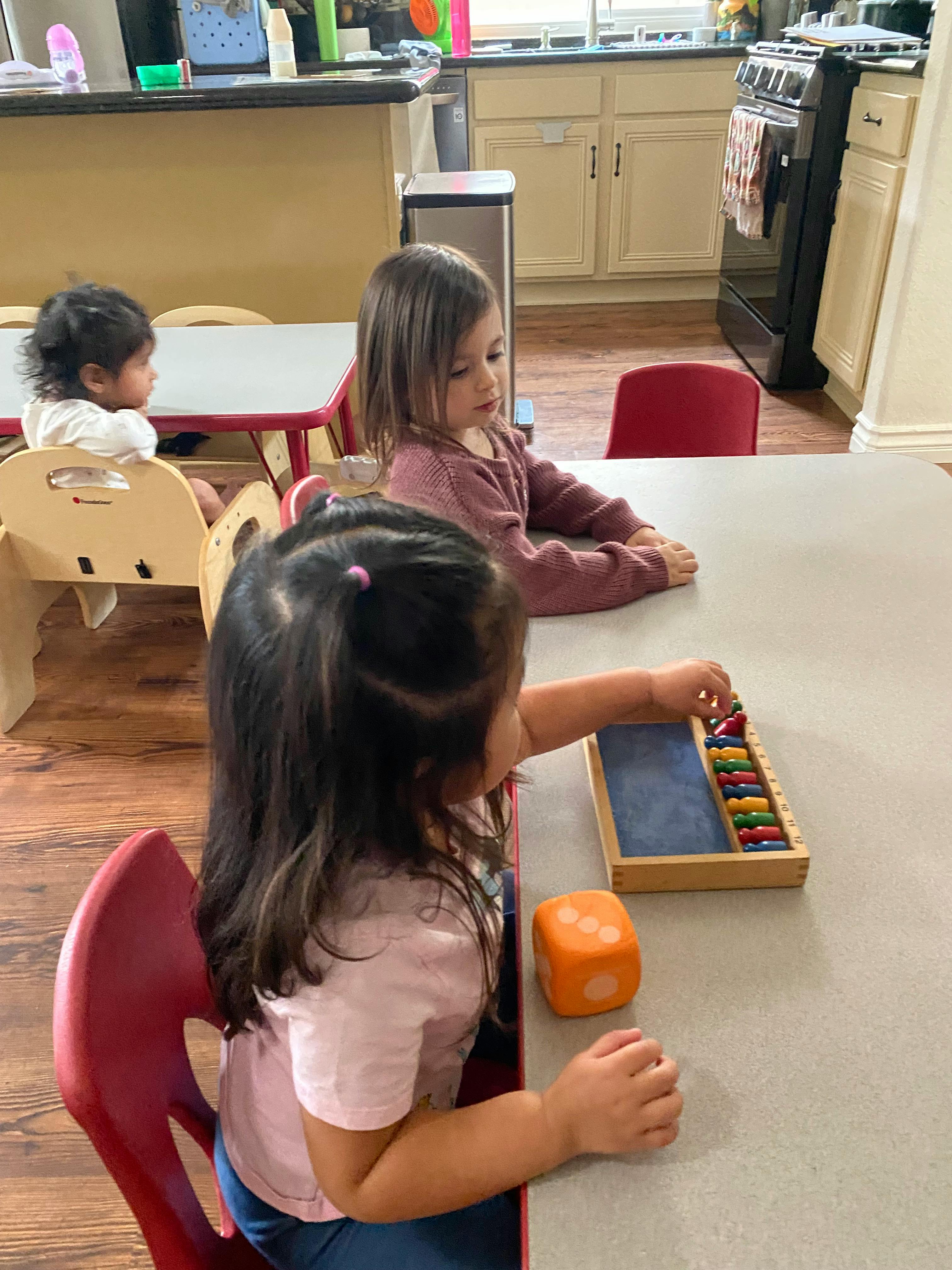 Three children sitting at tables, one playing with an abacus