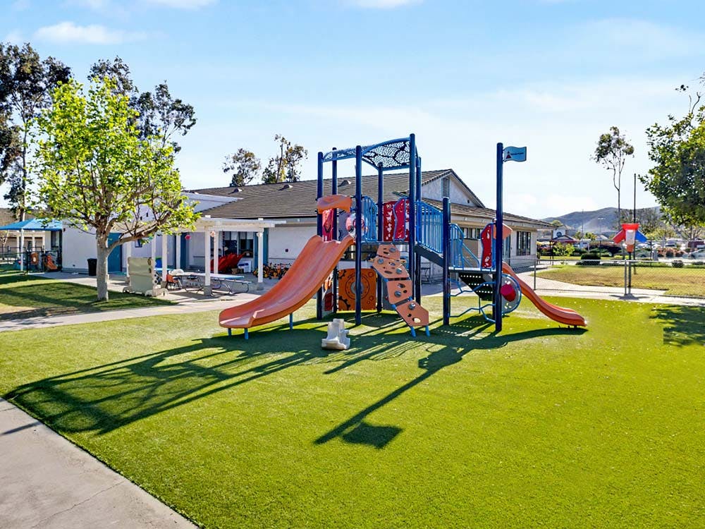 A playground with orange slides and blue climbing structures on green artificial turf
