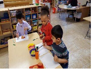 Three children drawing and crafting at a table in a classroom