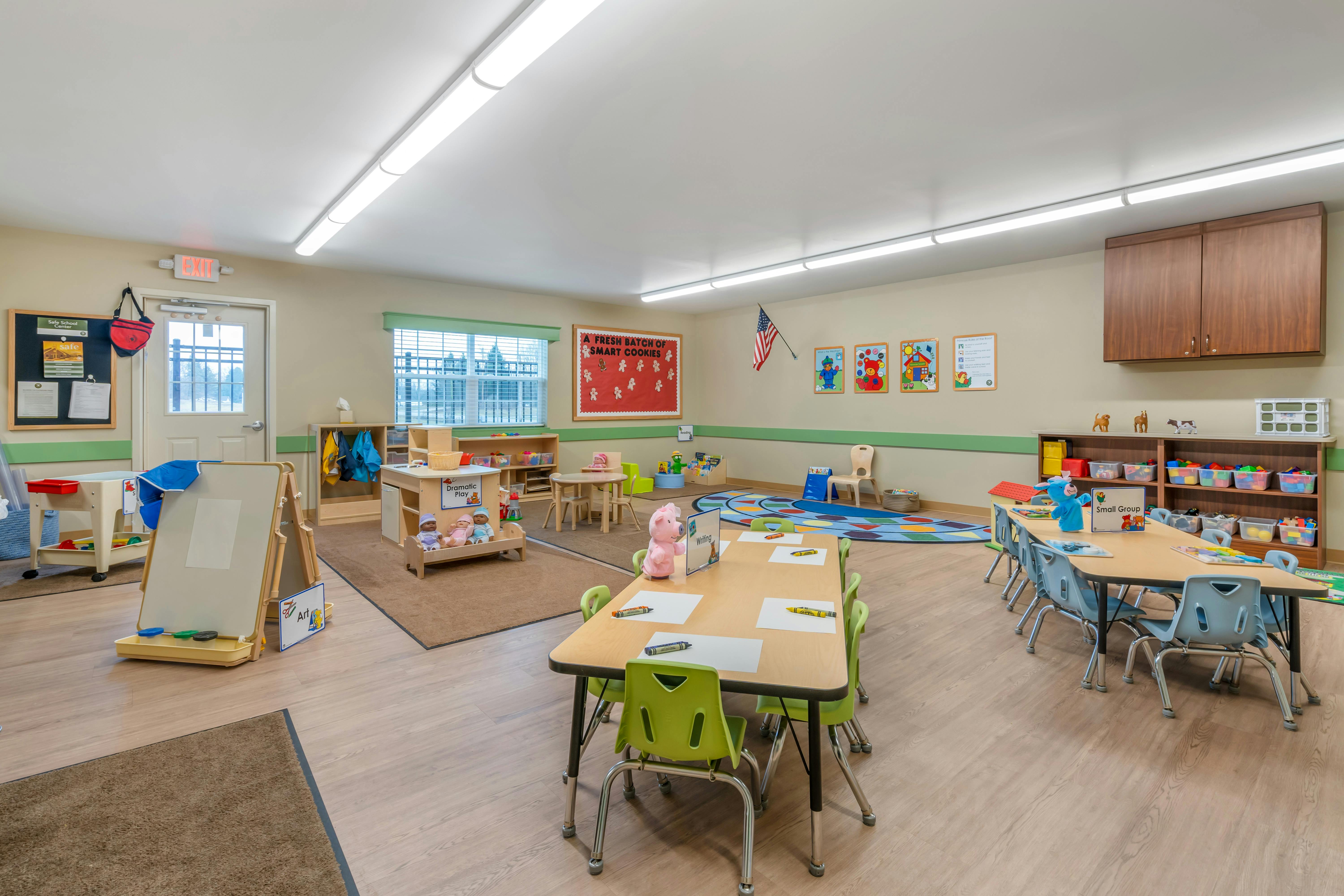 A classroom with small tables and chairs, a play area, and an art easel