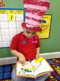 Child wearing a tall striped hat and bow tie, reading a book