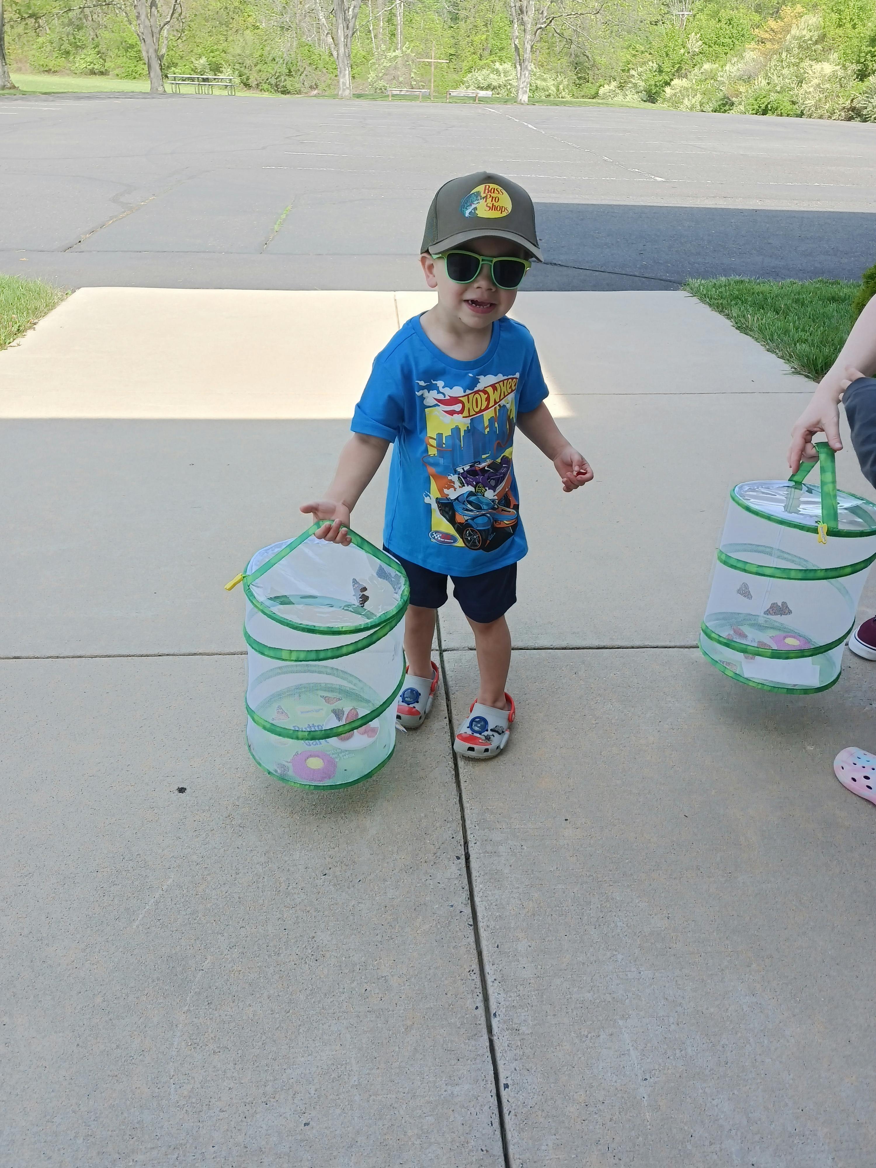 Child wearing sunglasses and a hat holding a butterfly habitat