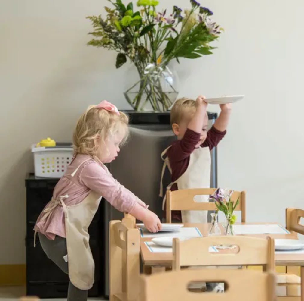 Two children in aprons setting a table with plates