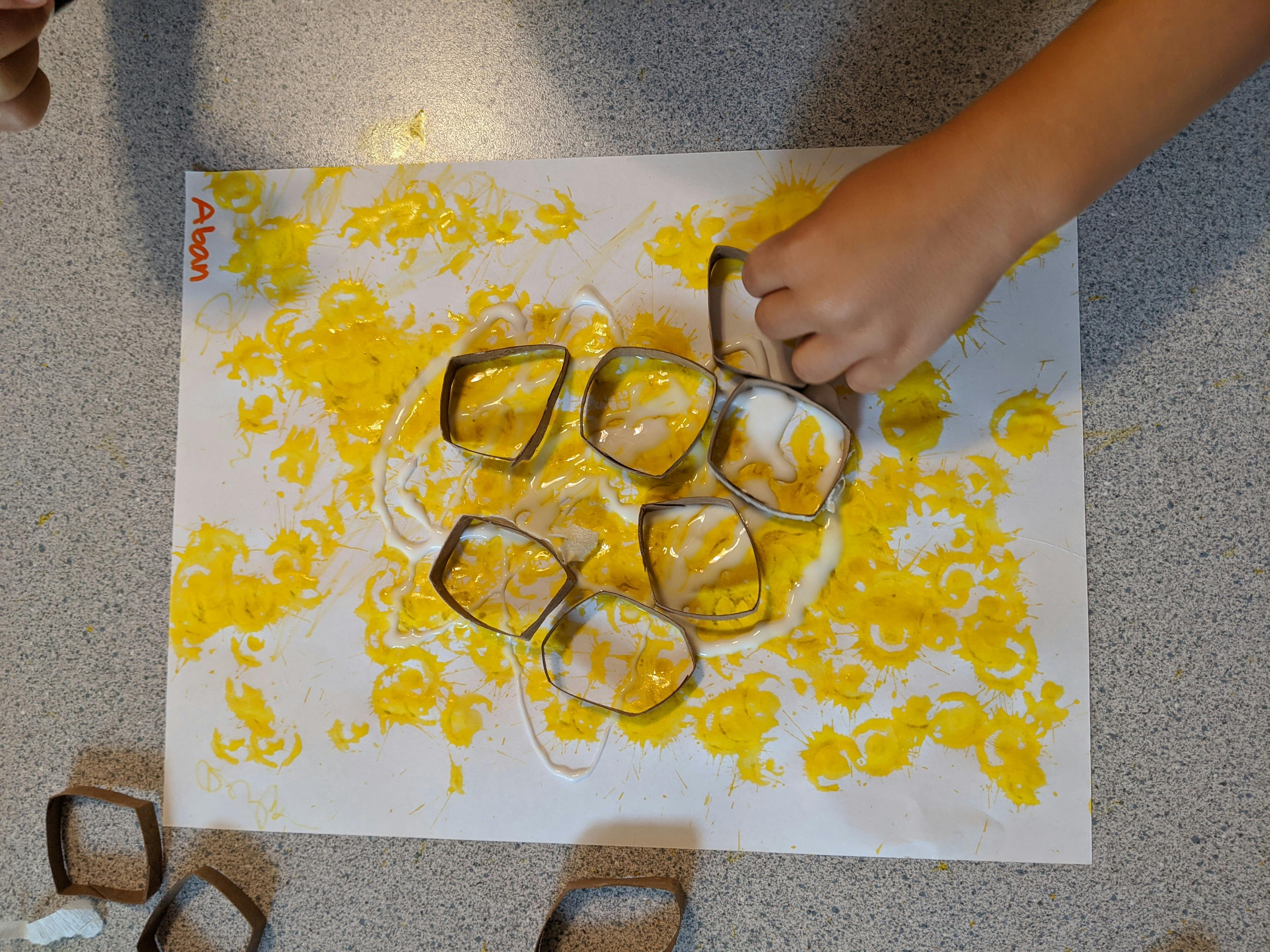 Child's hand pressing a cookie cutter into yellow paint on paper