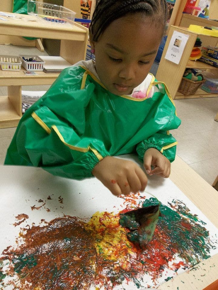 Child in a green smock painting with a cardboard tube