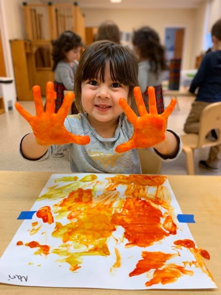 Child with orange paint on hands and paper
