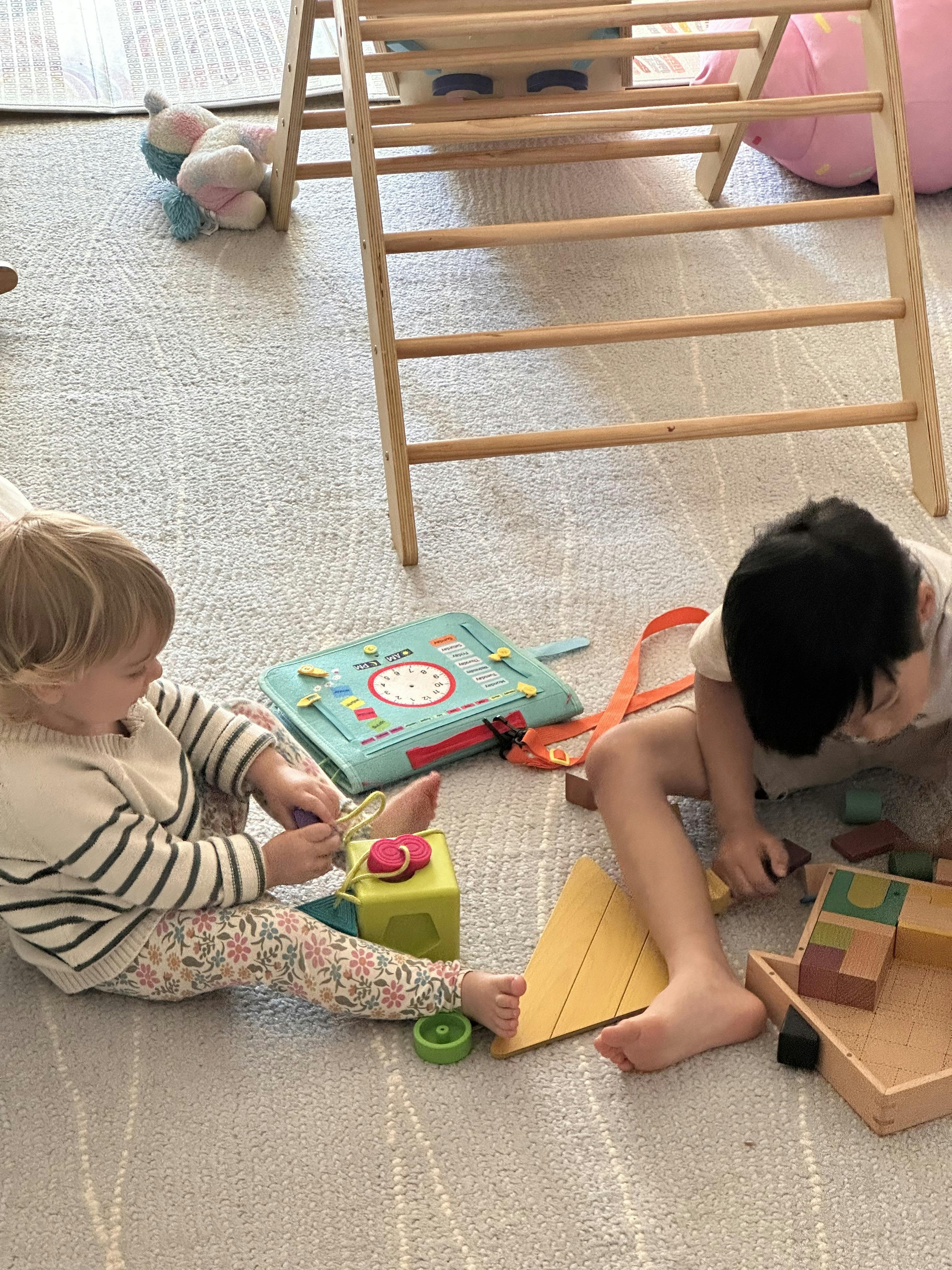 Two children playing on a rug with toys and building blocks